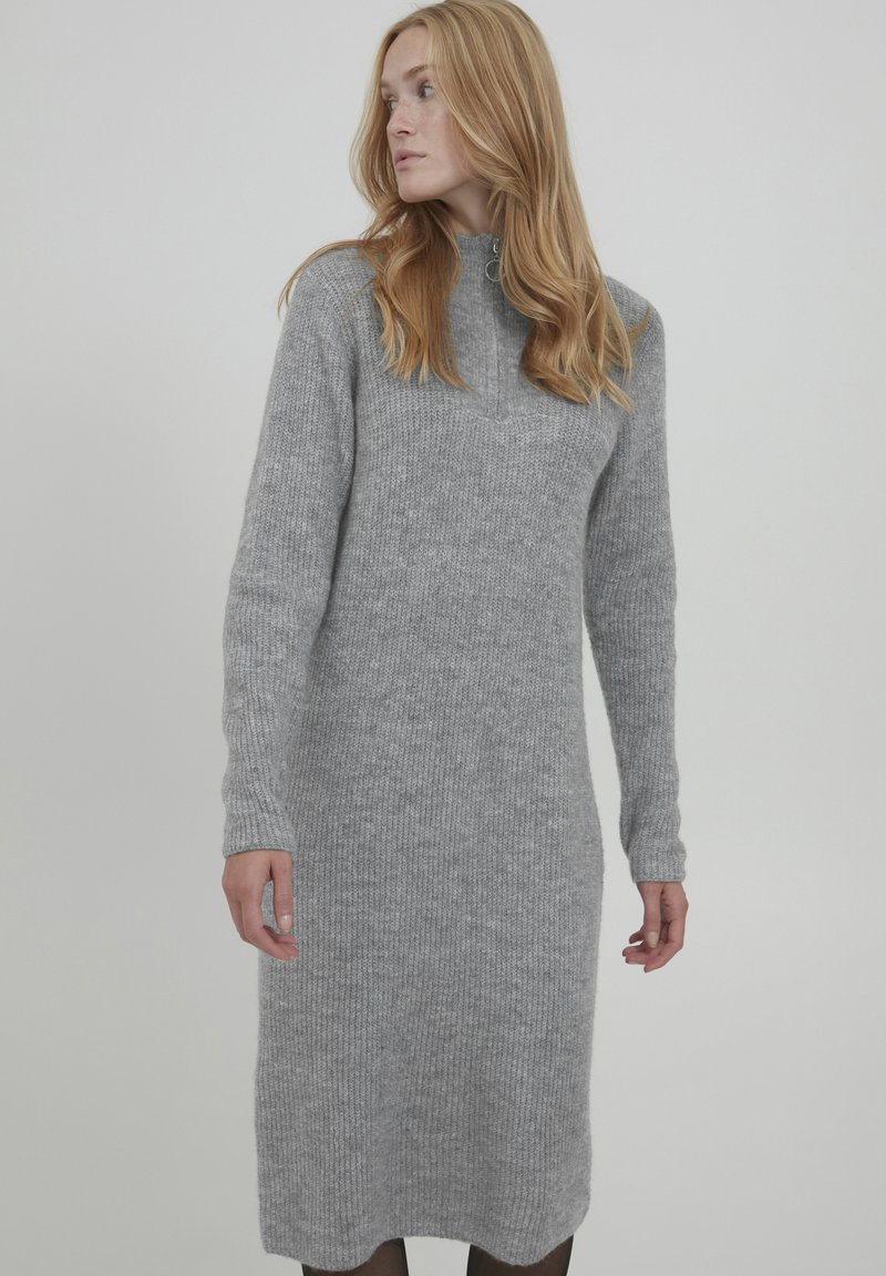 Abito grigio a maniche lunghe e collo alto, realizzato in tessuto a maglia testurizzata, lunghezza al ginocchio con una vestibilità rilassata. Presenta polsini a coste e un dettaglio con zip.