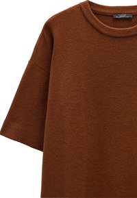 Brązowy sweter z dzianiny, z krótkimi rękawami, prążkowanym dekoltem i dołem. Gładka tekstura, casualowy krój i jednolity kolor na całej powierzchni.