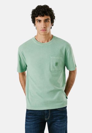 T-shirt mint verde a maniche corte realizzato in cotone morbido, con una tasca frontale con etichetta. Collo a giro classico, vestibilità rilassata.