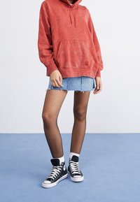Sudadera con capucha teñida de rojo, minifalda vaquera, medias de red y zapatillas negras de caña alta con suelas blancas. Detalles de un conjunto urbano informal visibles.