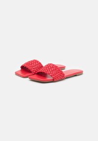 Sandales à glissière en jute rouge avec une semelle plate, dotées de deux larges sangles tressées. Texture lisse et design minimaliste sans ornement.
