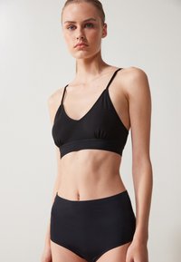 Svart bralette med V-hals, tynne justerbare stropper og et tettsittende underband, kombinert med høy-midje svart undertøy. Glatt stofftekstur.