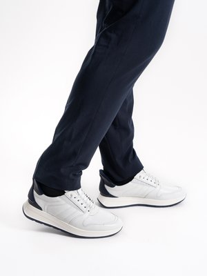 White and navy sneakers worn with dark navy pants against a plain white background, showing legs mid-step.