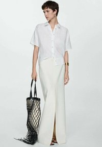 White linen short-sleeve shirt with a button front, paired with a long, cream skirt featuring a side slit. Black netted tote bag.