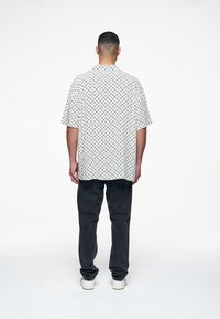 Camicia a maniche corte con colletto in tessuto bianco con motivo geometrico nero; abbinata a jeans scuri e sneaker bianche.