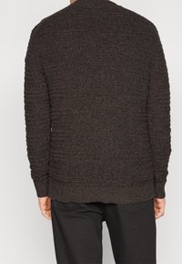 Maglione lavorato a maglia marrone con motivo a costine, maniche lunghe e scollatura arrotondata. L'orlo è leggermente più lungo sul retro.