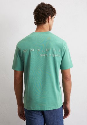T-shirt in cotone verde con maniche corte, collo a giro e coordinate stampate sul retro, insieme a un logo in un colore contrastante.