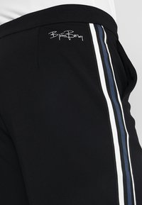 Svarta träningsbyxor med en slät textur, med kontrasterande vita och blå ränder längs sidorna och en liten broderad logga på höften.