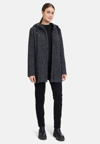 Szary, teksturowany płaszcz z kapturem, z zapięciem na zamek i dwoma bocznymi kieszeniami. Noszony na czarną bluzkę i spodnie, zestawiony z czarnymi, masywnymi butami.
