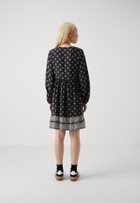 Μαύρο φόρεμα με μακριά μανίκια και λευκά γεωμετρικά σχέδια, συγκεντρωμένη μέση και υφή στο τελείωμα. Φοριέται με μαύρες κάλτσες και λευκά αθλητικά παπούτσια.