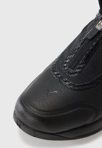 Czarne buty sportowe z teksturowaną powierzchnią, zamkiem błyskawicznym, amortyzowaną podeszwą i małym logo po boku. Gładkie i trwałe materiały.