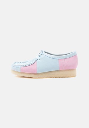 Zapato bajo con paneles de ante en azul pastel y rosa, suela de goma crepé beige, puntera redondeada y cordones blancos sobre un fondo blanco.