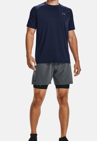 Laivastonsininen urheilupaita lyhyillä hihoilla yhdistettynä harmaisiin shortseihin. Materiaalina kosteutta siirtävä kangas ja istuva muotoilu. Molemmissa vaatekappaleissa on logot.