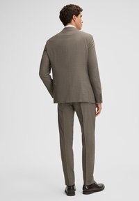 Szary garnitur w kratę o dopasowanym kroju, marynarka jednorzędowa i spodnie z prostymi nogawkami, zestawione z ciemnymi butami. Widok od tyłu.