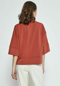 Rustrød cropped top med korte ærmer, som har en afslappet pasform og en glat tekstur. Enkel design uden yderligere mønstre eller metaldele.