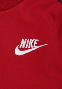 Tela roja con cuello acanalado, que presenta un logotipo de Nike bordado en blanco con un diseño de swoosh. Textura suave, detalles mínimos.