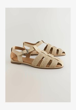 Beige nahka sandaalit, joissa on kudottu kuvio varpailla ja säädettävä nilkkaremmi. Litteä pohja, jossa on minimaalinen varusteiden korostus.