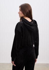 Sort cropped hoodie med hætte, der har en blød tekstur og lange ærmer. Parret med matchende sorte bukser for et koordineret look.