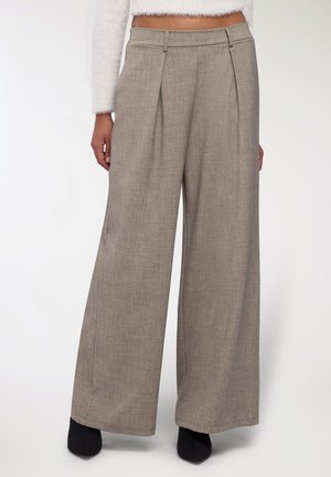 Pantaloni a gamba larga in tessuto grigio chiaro a zigzag con pieghe frontali, dotati di una vita strutturata e tasche laterali. Tacchi neri completano il look.