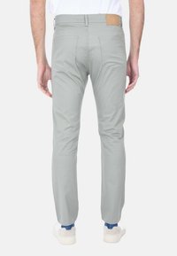 Pantaloni slim-fit grigio chiaro realizzati in misto cotone, con due tasche posteriori e una patch in pelle beige sulla vita, abbinati a sneakers bianche.
