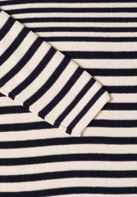 Marineblauwe en crèmekleurige gestreepte gebreide stof met getextureerde ribbels. Bevat een mouw met zichtbare naad en contrasterende kleurpatronen.