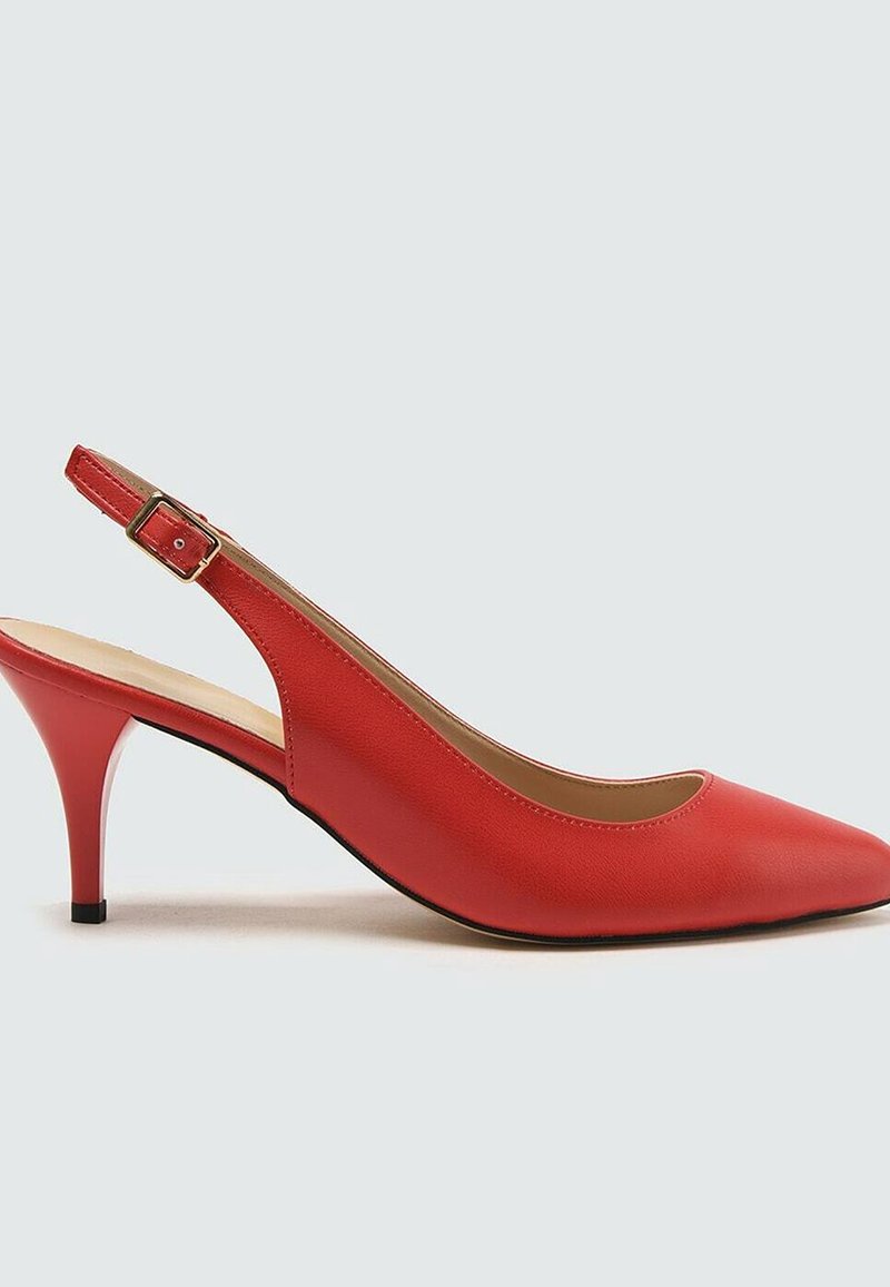 Escarpin haut en cuir rouge à bride arrière avec un bout pointu et une boucle dorée sur la sangle de la cheville, sur fond uni.