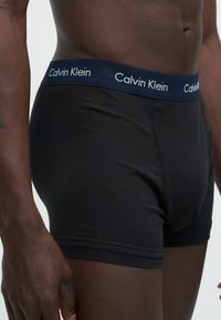 Ανδρικός κορμός με μαύρα μποξεράκια Calvin Klein με σκούρο μπλε ζώνη και λευκό λογότυπο Calvin Klein.