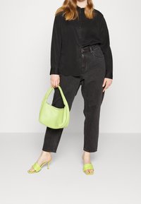 Schwarze Button-up-Hemd, dunkle Jeans, grüne strukturierte Handtasche und knallgrüne Riemchenmules, die eine Mischung aus lässigen und lebhaften Elementen präsentieren.