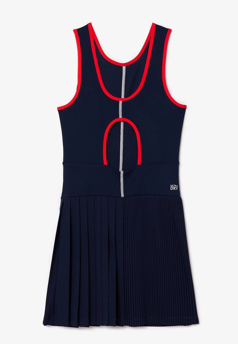 Marineblauwe sportieve jurk met rode accenten. Heeft een mouwloze ontwerp, een geplisseerde rok en een uitsnijding op de rug. Gemaakt van vochtregulerende stof.