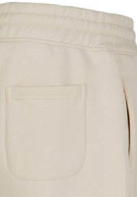 Beige joggebukser med ribbet midje, sidelommer og en baklomme med sømkanter. Myk tekstur og uformell design.