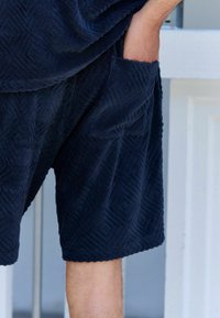 Pantalones cortos de rizo azul marino que presentan un patrón geométrico texturizado, bolsillo lateral y un corte relajado. Material suave con tela en bucle.