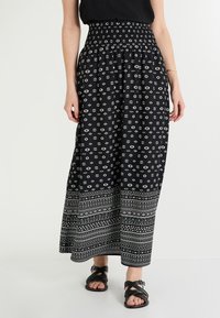Falda maxi negra con cintura fruncida, que presenta patrones en forma de diamante y geométricos en blanco, y un dobladillo con líneas horizontales.  