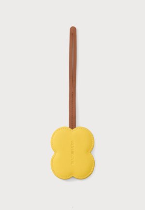 Étiquette en cuir jaune en forme de fleur avec une lanière marron, "marimekko" embossé au centre de l’étiquette.