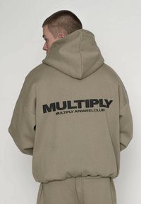 Beżowa, oversize bluza z kapturem z dużym czarnym logo „MULTIPLY” oraz napisem „MULTIPLY APPAREL CLUB” na plecach. Miękki, teksturowany materiał.