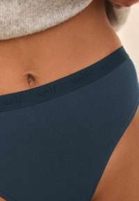 Slip bikini in cotone blu scuro con una morbida fascia in vita caratterizzata dal testo "self." in un motivo ripetuto. Texture liscia, design a vita media.