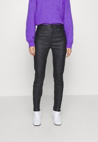 Pantalones de imitación de cuero negros con detalles ribeteados en los muslos, combinados con un suéter púrpura y botas blancas hasta el tobillo.
