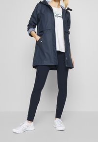 Mörkblå vattentät jacka med huva, tryckknappar och randig foder. Matchas med mörkblå leggings och vita sportskor.