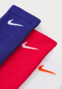 Tre par ribbede sokker i marineblå, rød og hvit, hver med en kontrasterende Nike-logo i hvit eller oransje.