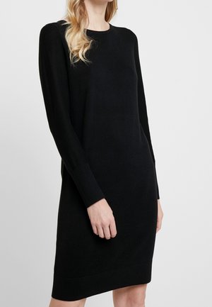 Zwarte gebreide jurk met lange mouwen, ronde hals en ribbels aan de mouwen. Gladde textuur, knielengte, minimalistisch ontwerp zonder patronen of accenten.