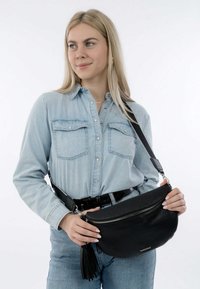 Zwarte leren schoudertas met een gestructureerde afwerking, ovale vorm, zilveren rits en een franjesaccent. Gekleed met een glanzende zwarte riem.
