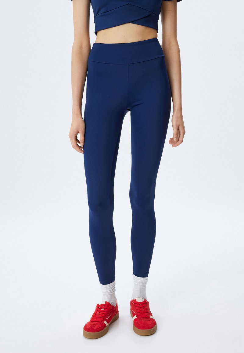 Marinblå leggings i stretchigt tyg, hög midja, kombinerade med röda skor och vita ankelsockor. Nära passform och slät textur.