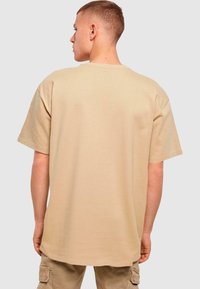 Beige oversized T-shirt lavet af bomuld, med en standard rund hals og korte ærmer, der viser en ensartet, glat struktur.