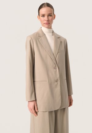 Beige blazer with notched lapels, two buttons, and a single chest pocket; made of smooth fabric; paired with a high-neck top.