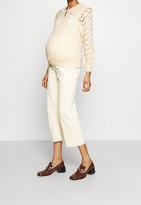 Krämfärgad stickad tröja med bred krage, kombinerad med off-white avklippta byxor och glansiga bruna blockklackskor.