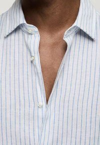 Jasnoniebieska koszula w białe paski z lnu z kołnierzykiem zapinanym na guziki oraz luźnym krojem, z widocznymi guzikami i miękką teksturą.