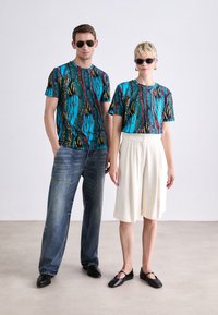 Mønstret grafiske t-shirts i flere farver med blå, rød og gul, parret med lyse shorts og mørke jeans samt sorte sko.