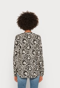 Camicia a maniche lunghe realizzata in tessuto con un motivo floreale bianco e nero. Presenta un collo rotondo e una linea dritta con un dorso più lungo.