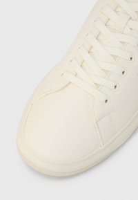 Λευκό δερμάτινο αθλητικό παπούτσι με επίπεδα κορδόνια, στρογγυλεμένη μύτη, υφή στο  πάνω μέρος και διακριτικές ραφές. Εξωτερική σόλα από λάστιχο με ελαφρύ μοτίβο πρόσφυσης.