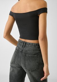 Musta olkapäät paljastava lyhyt yläosa, yhdistetty korkeavyötäröisiin tummanharmaisiin farkkuihin. Yläosassa on sileä pinta, ja farkuissa on kulunut ilme.