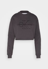 Tumši pelēks īsais džemperis ar garām piedurknēm, ar teksturētu melnu "Calvin Klein Jeans" logotipu priekšpusē. Izgatavots no kokvilnas maisījuma.